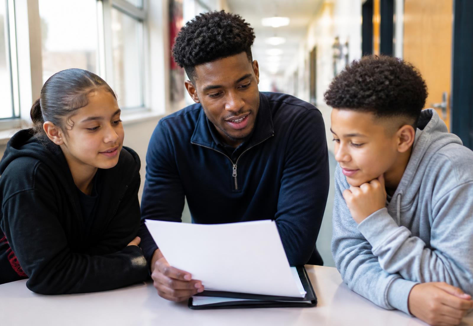 A mentor reviewing a student progress plan with two middle-school students